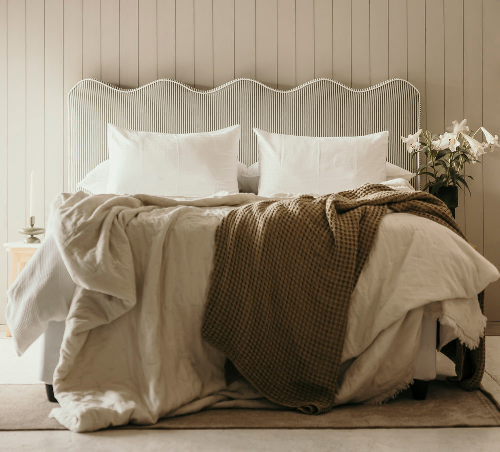 Neatly made bed with white pillows and a brown throw blanket in a bedroom setting.