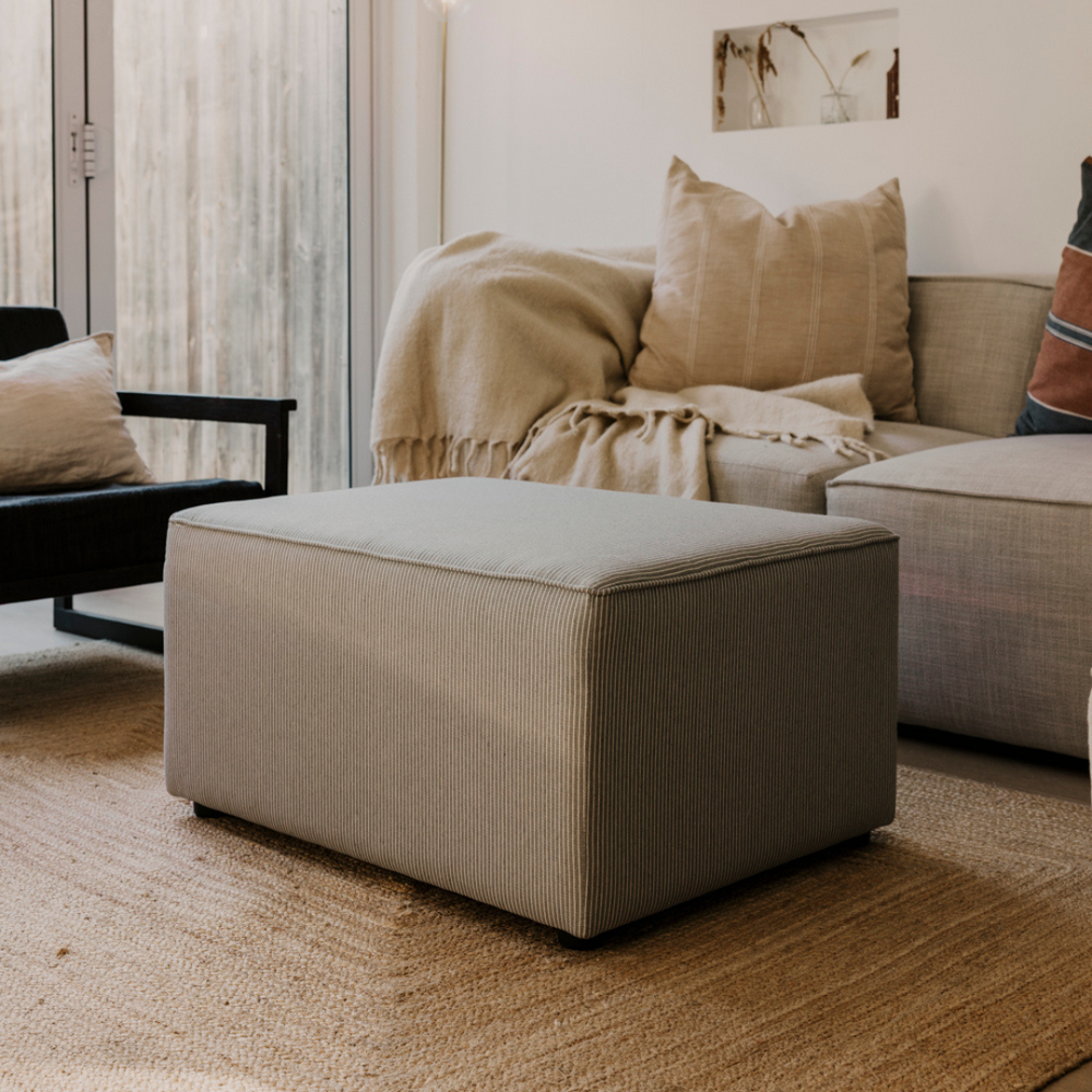 Beige ottoman in a living room setting with a sofa and cushions.