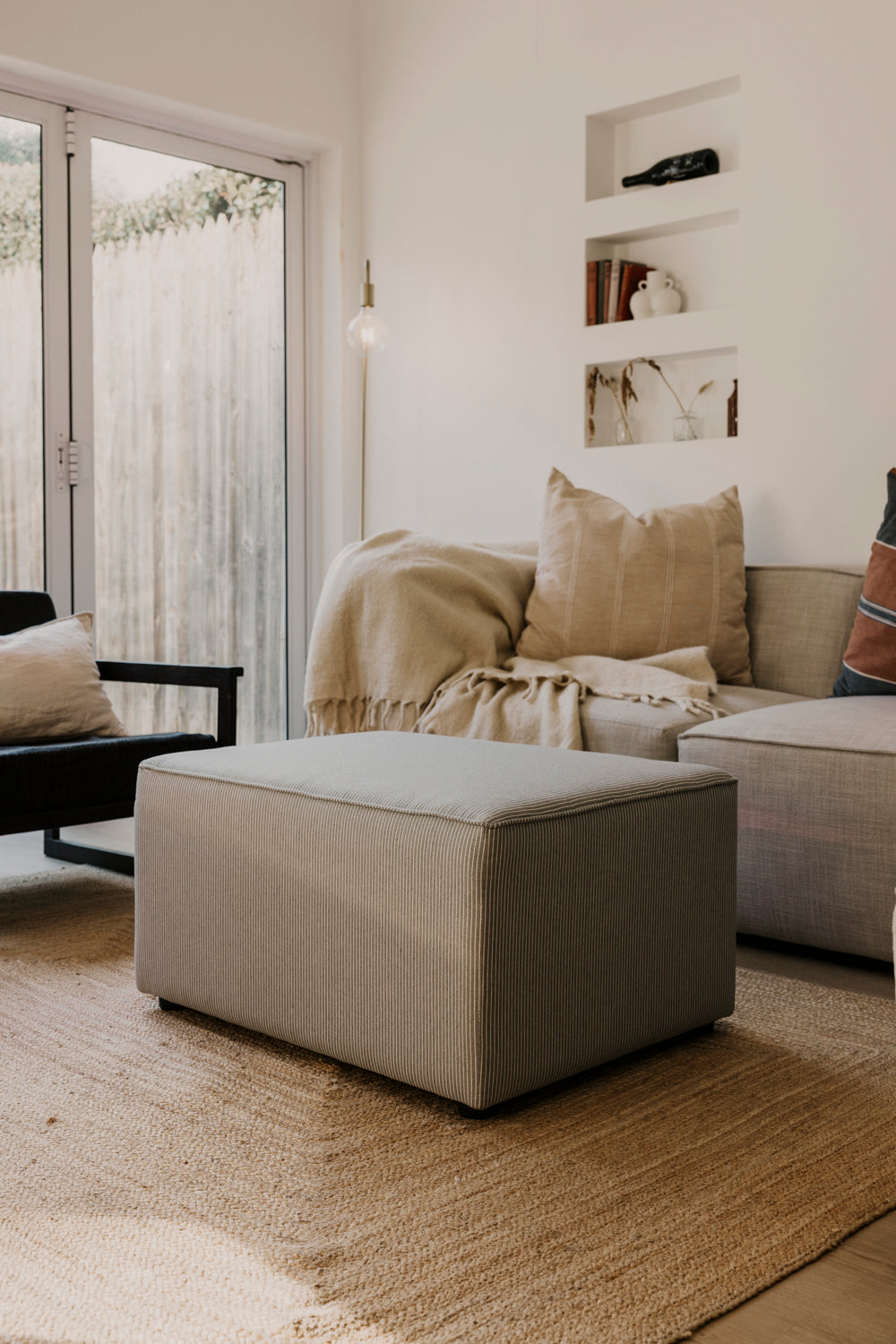 Modern living room with beige sofa, ottoman, and decorative pillows.