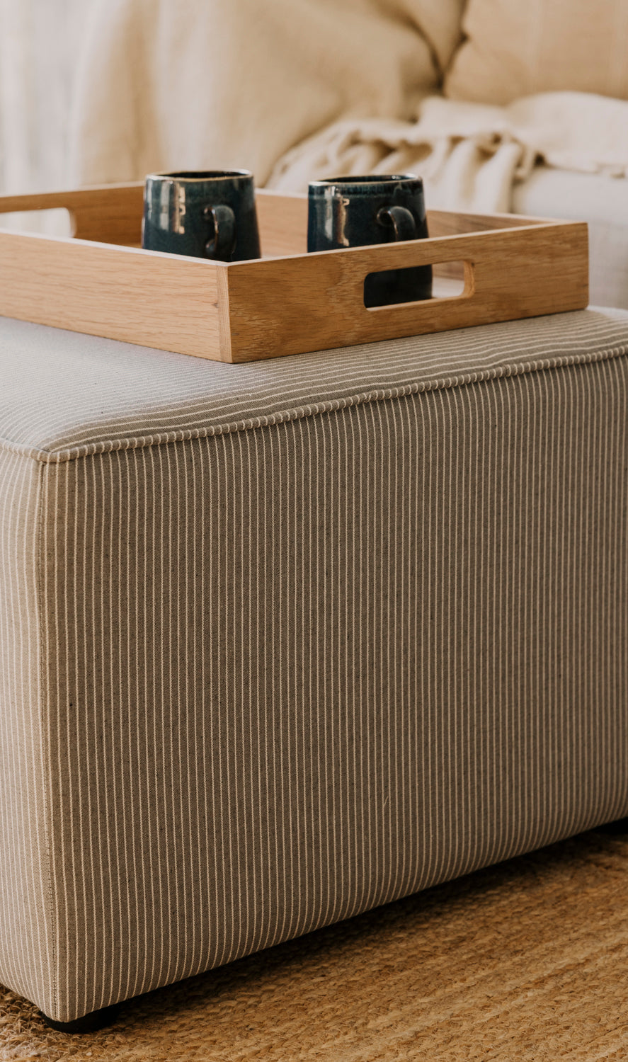 Wooden tray with two black containers on a beige ottoman.