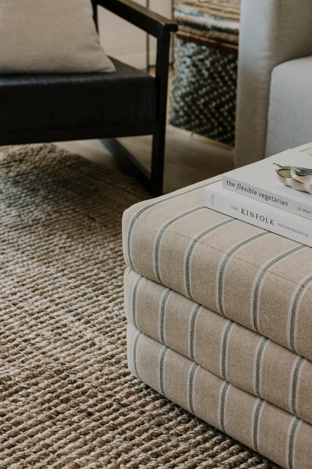 Stack of books on a striped ottoman in a living room setting