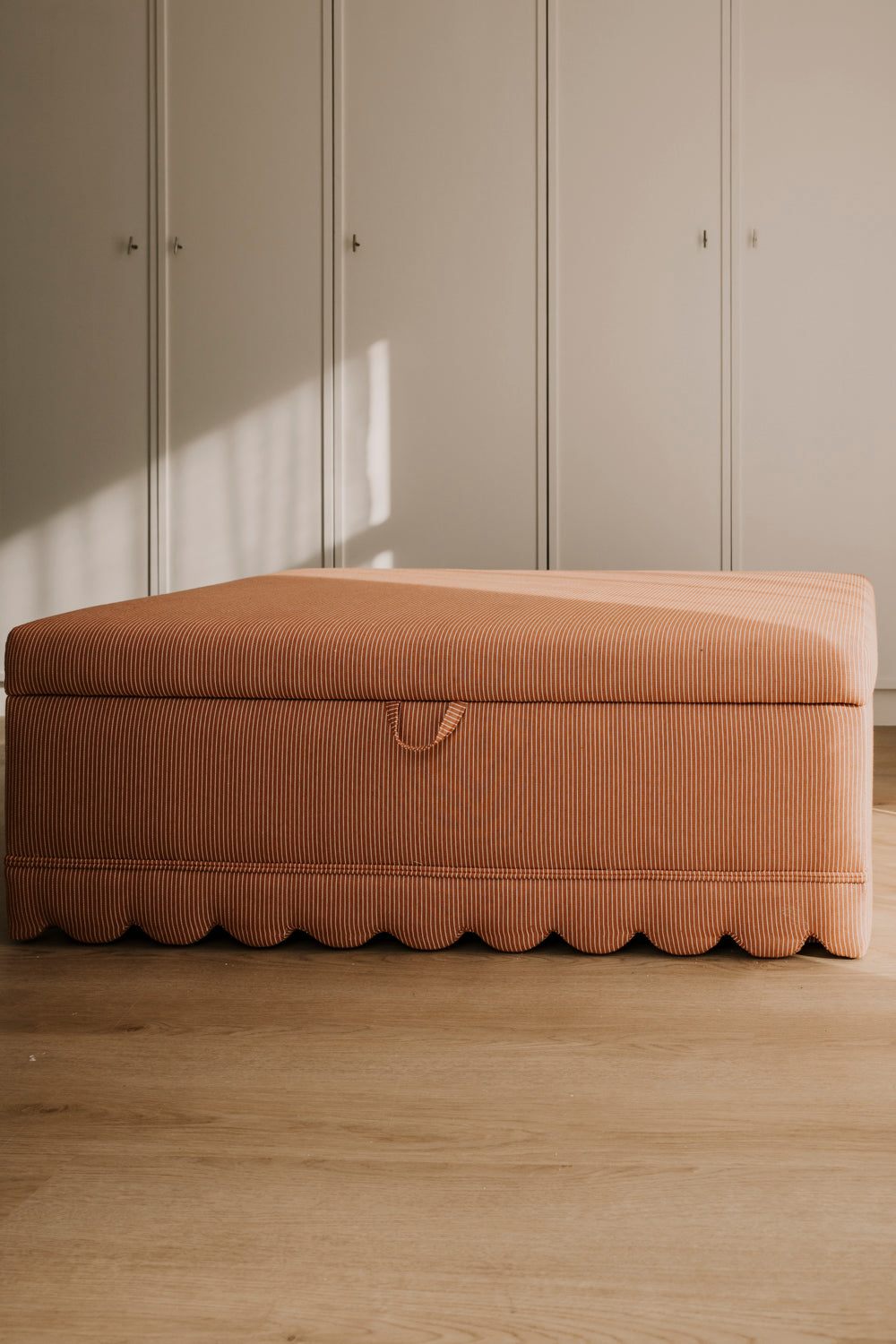 Brown ottoman against a neutral wall with wooden flooring
