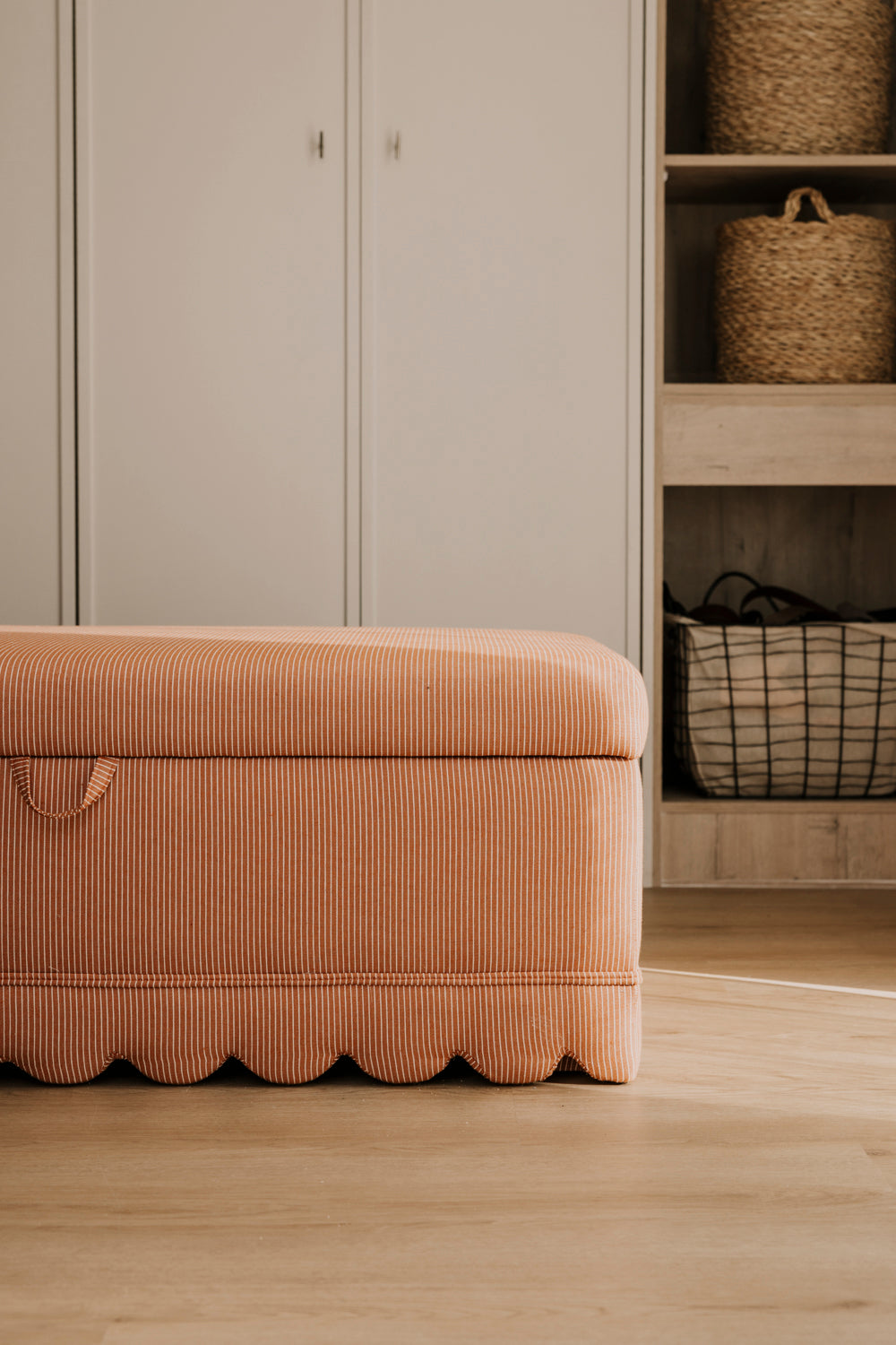Beige storage ottoman in a room with neutral-colored walls and wooden flooring.