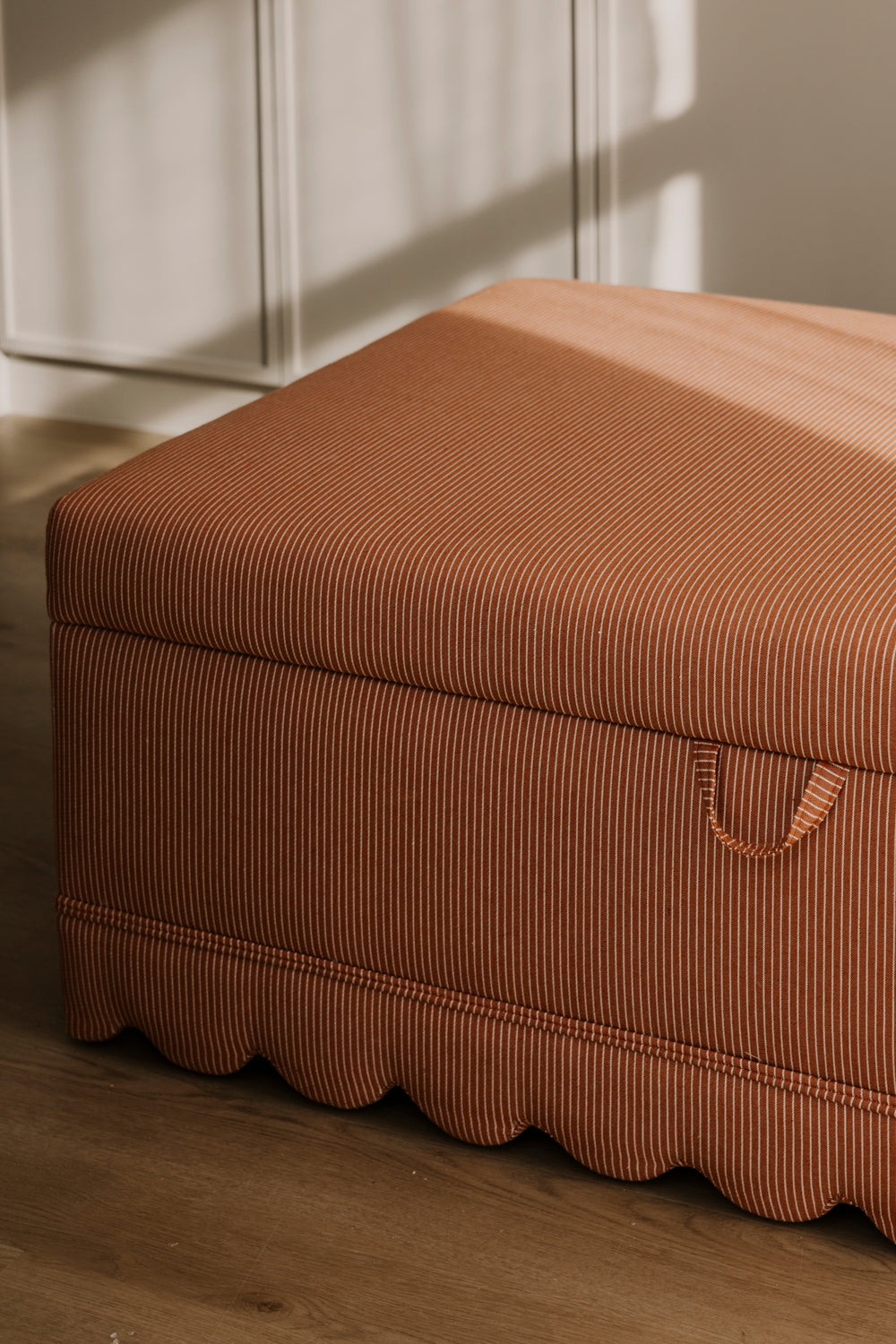 Brown ottoman with a textured surface on a wooden floor.