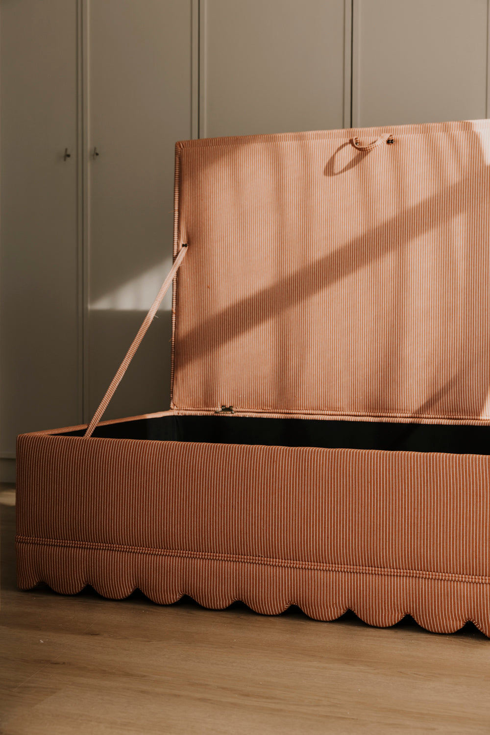 Brown storage box with a lid on a wooden floor against a neutral wall.