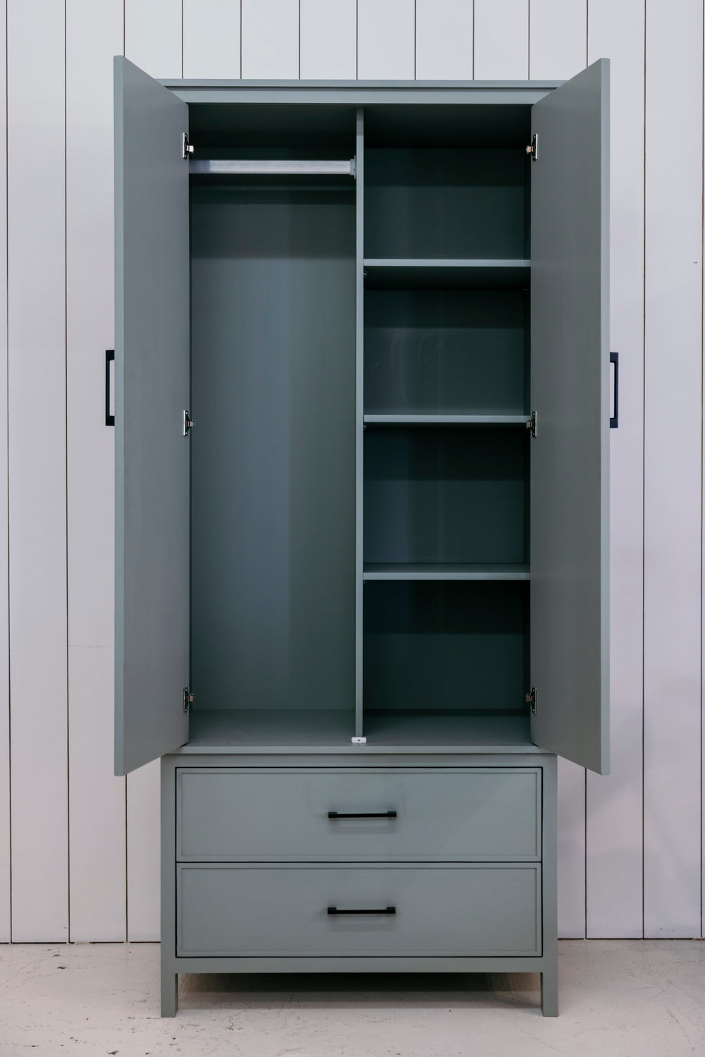 Gray wardrobe with open doors and drawers against a white paneled wall.