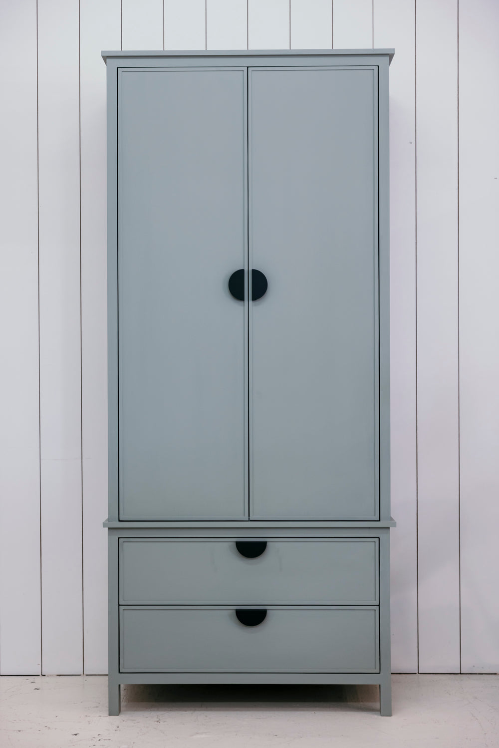 Gray wardrobe with black handles against a white paneled wall