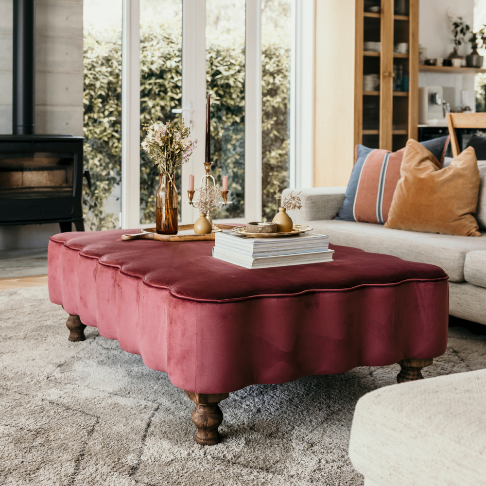 Living room with a maroon ottoman, books, and decorative items.