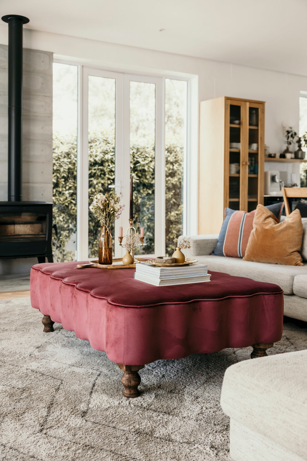 Living room with a red ottoman, white sofa, and large windows.