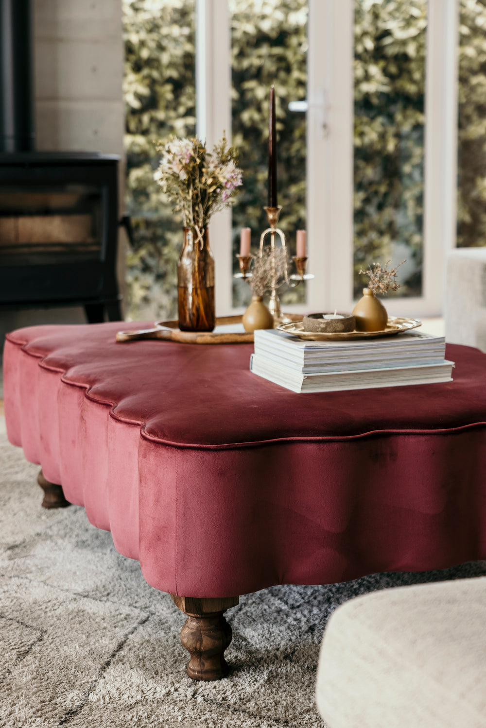 Maroon ottoman with decorative items in a room with large windows.