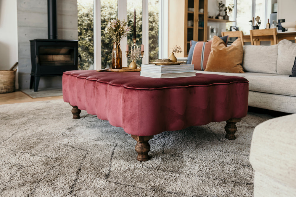 Maroon ottoman in a living room setting with books and decorative items.