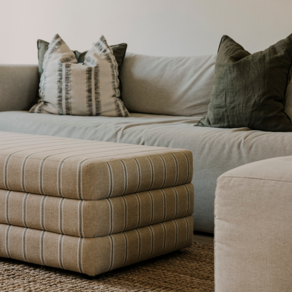 Beige sectional sofa with patterned cushions and a striped ottoman.