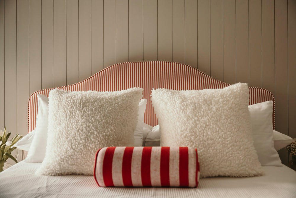 Bed with white pillows and a red and white striped bolster against a wooden panel wall.