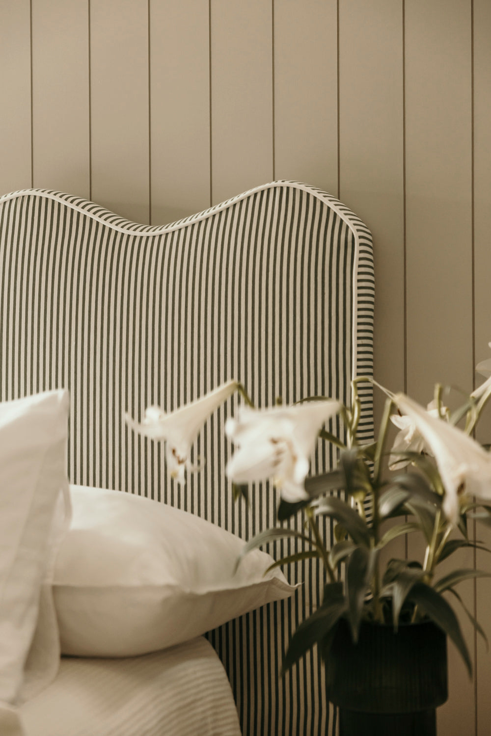 Striped headboard with pillows and a plant against a wooden panel wall