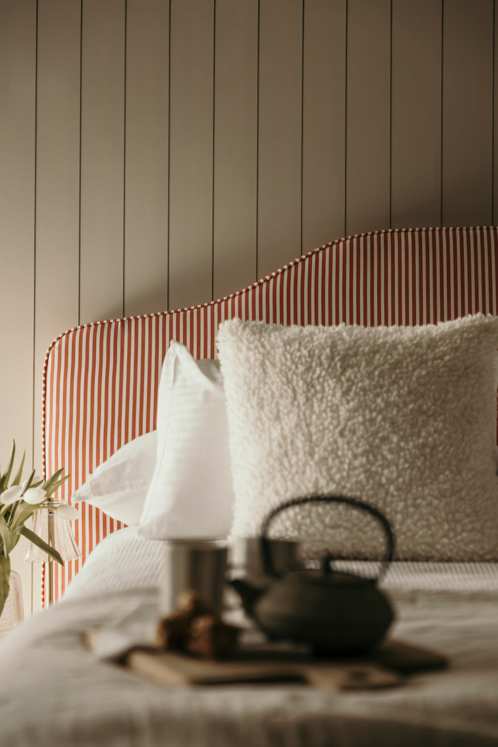 Tea set on a bed with striped headboard and pillows