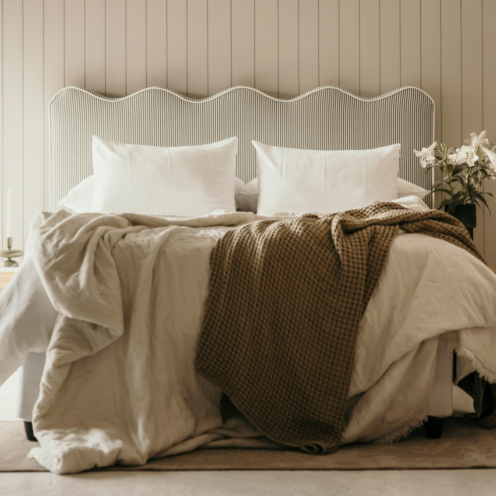 Neatly made bed with white bedding and a brown throw blanket against a wooden paneled wall.