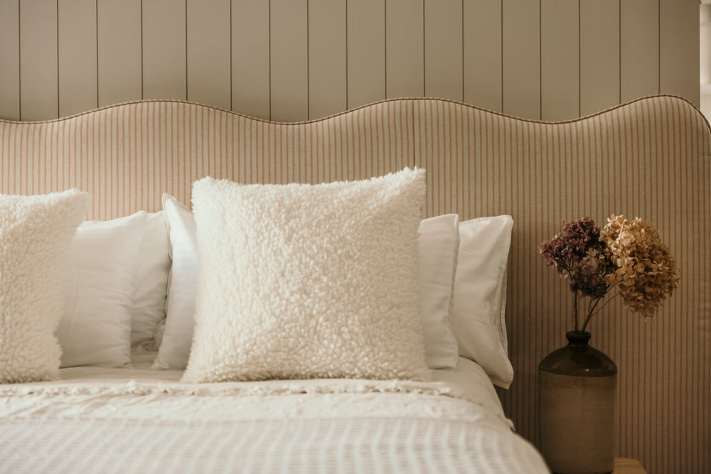 Neatly made bed with decorative pillows against a textured wall.