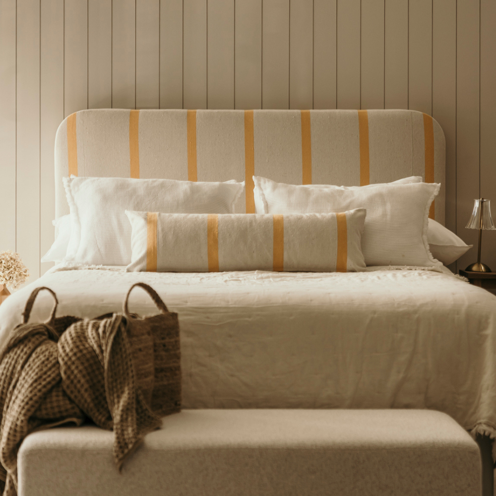 Beige bed with striped headboard and pillows against a wooden paneled wall.