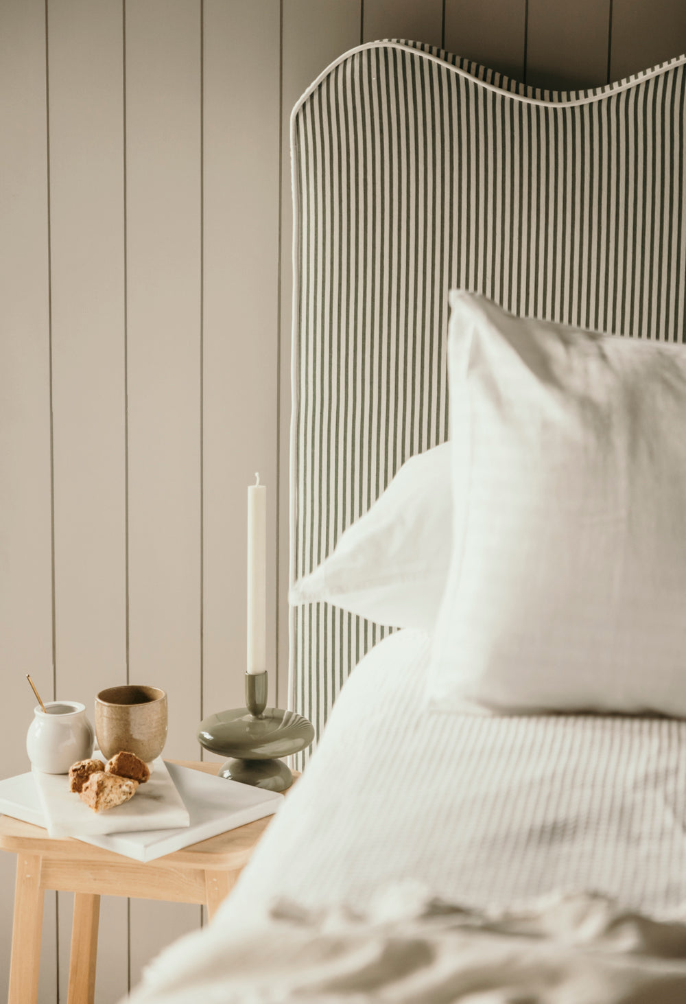 Neatly made bed with white bedding and pillows against a wooden headboard.