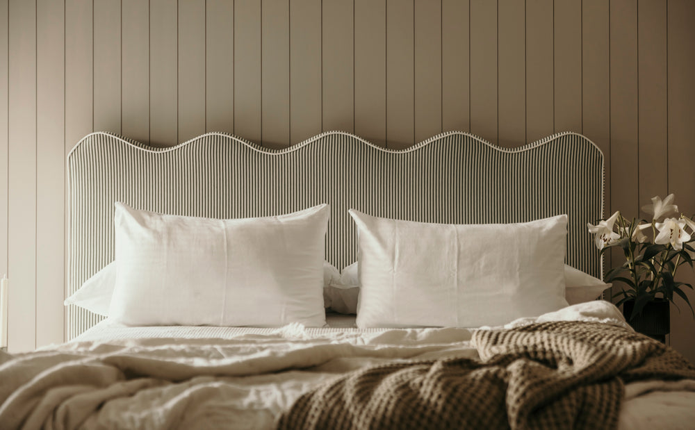Bed with white pillows and a textured headboard against a striped wall.