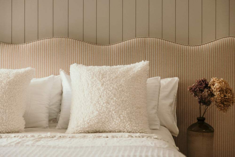 Neatly made bed with decorative pillows against a wooden panel wall.