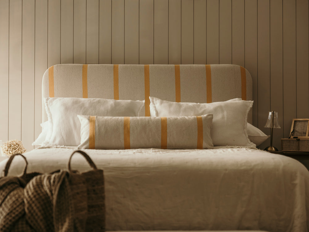 Bed with striped headboard and pillows against a wooden paneled wall.
