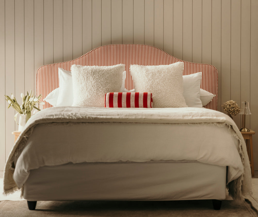 Neatly made bed with striped headboard and decorative pillows in a bedroom setting.