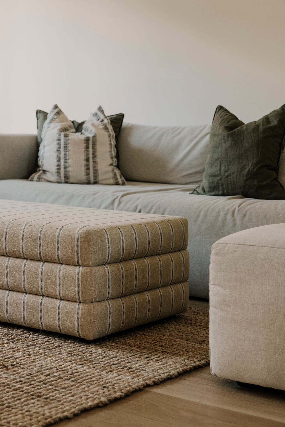 Beige sectional sofa with patterned and solid cushions on a wooden floor.