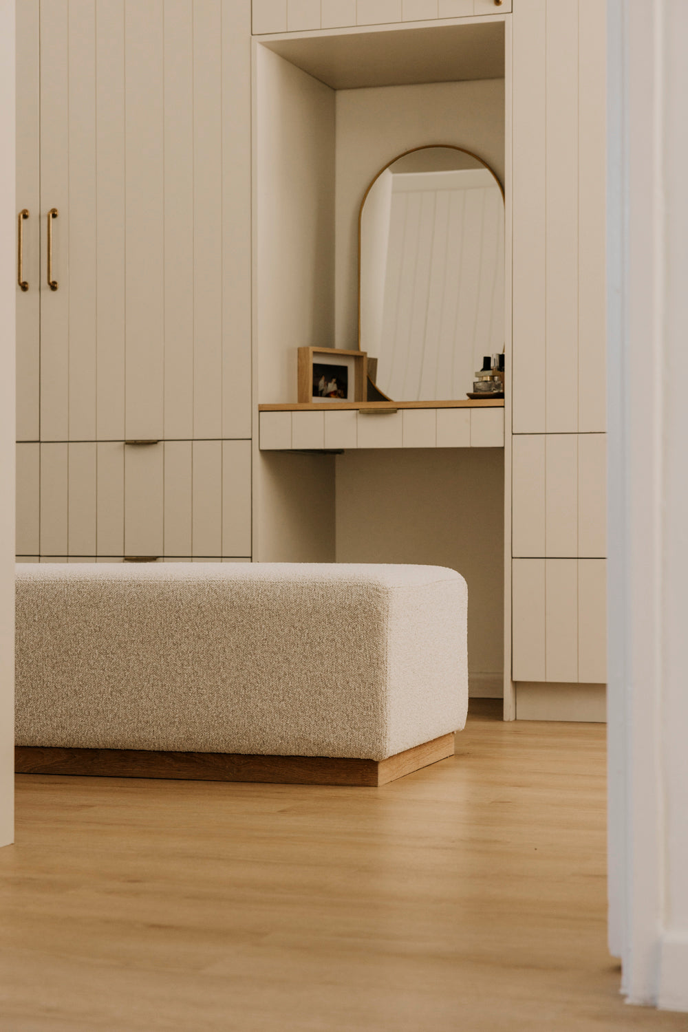 Beige wardrobe with a mirror and bench in a minimalistic room.