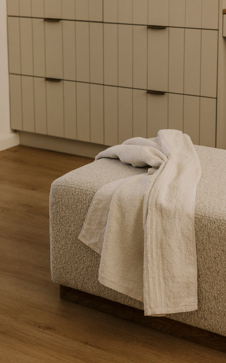 Beige towel draped over a textured surface with wooden flooring and neutral cabinets in the background