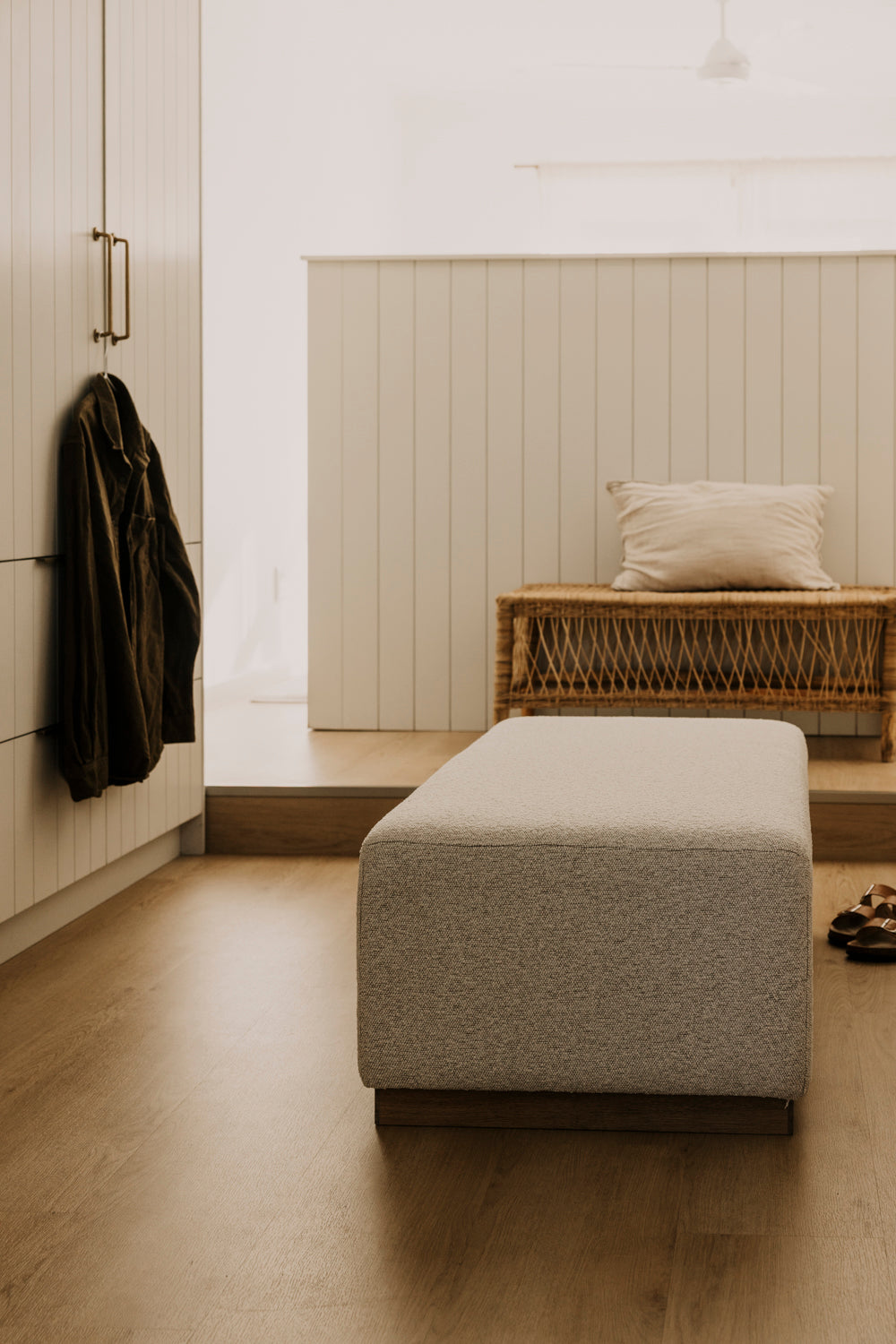 Modern interior with a gray ottoman, wooden bench, and coat on a white wall.