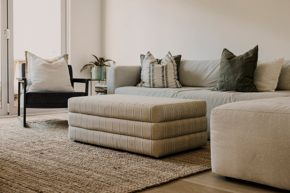 Beige sectional sofa with patterned ottoman in a living room setting.