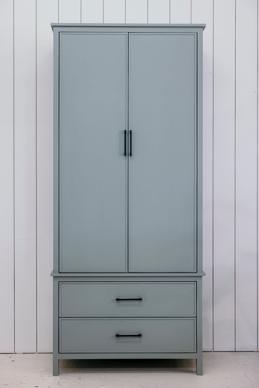 Gray wardrobe with two doors and two drawers against a white paneled wall.