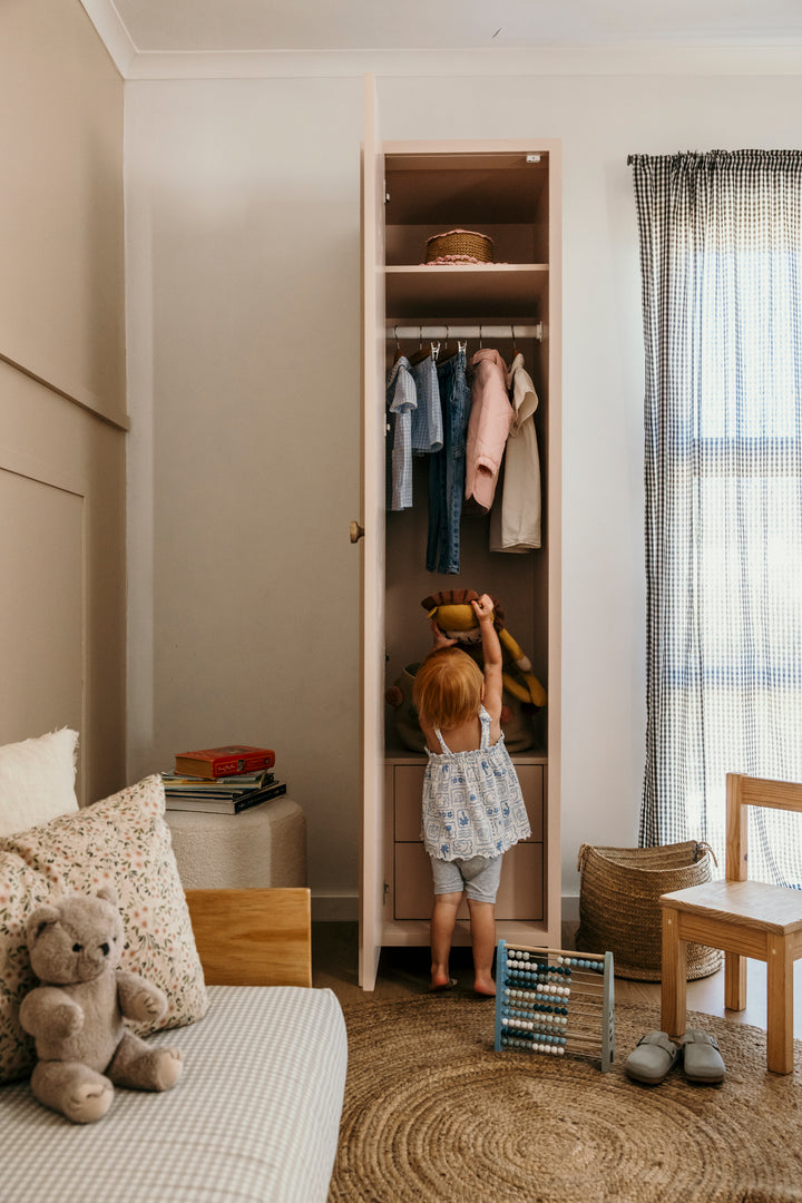 Child looking into an open closet with clothes in a bedroom.