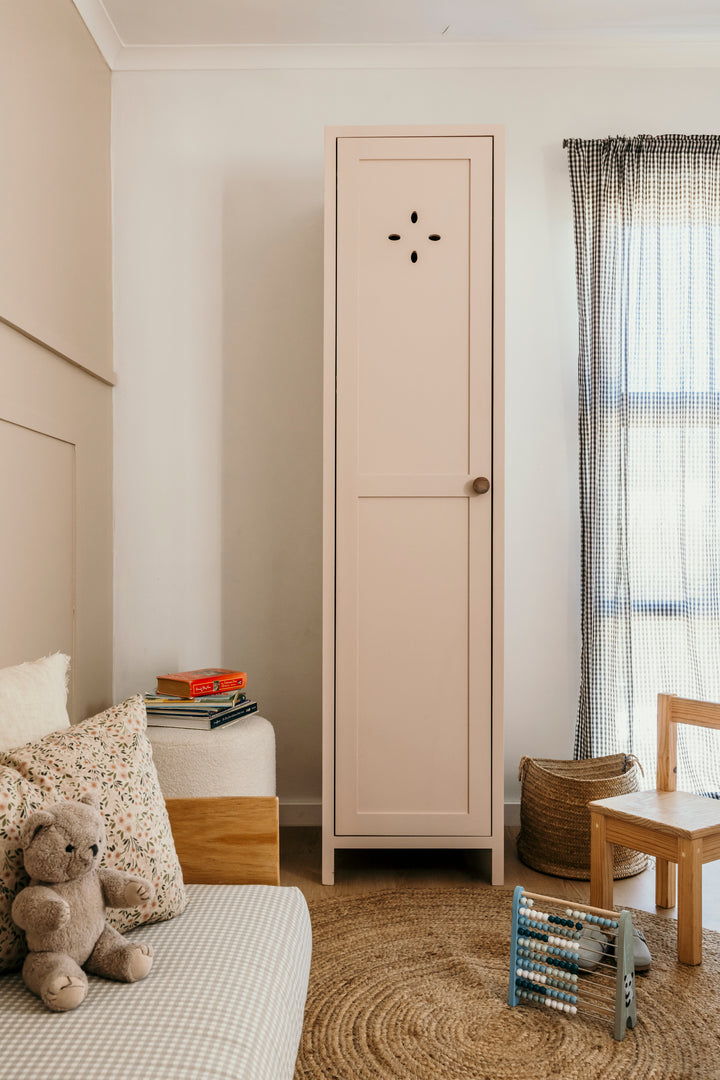 Beige wardrobe in a child's bedroom with a teddy bear, books, and a chair.