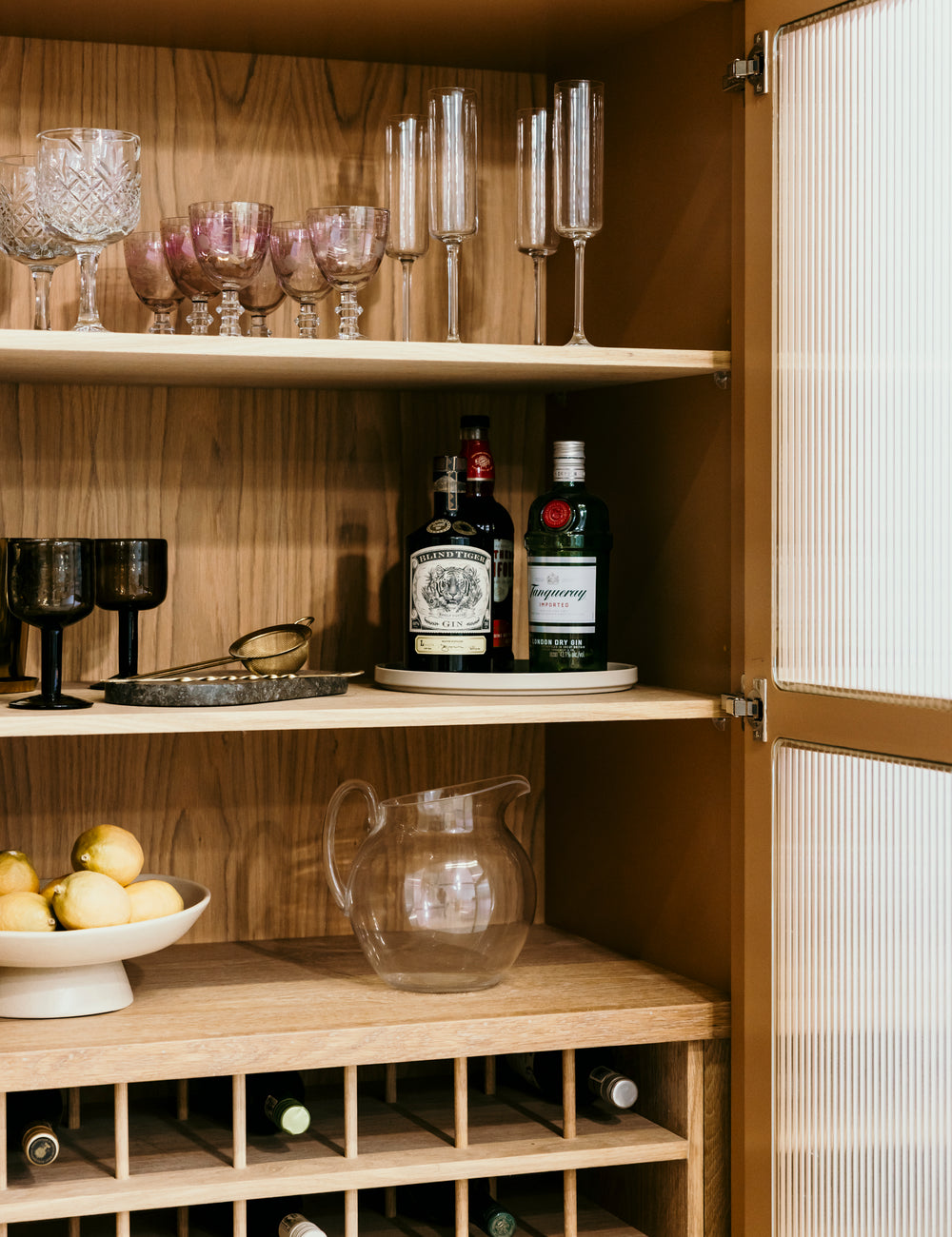 Wooden bar cabinet with liquor bottles, glasses, and a pitcher.