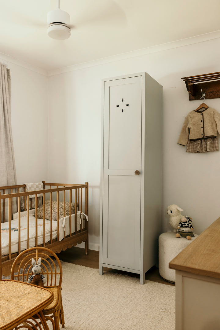 Nursery room with wooden crib, tall white locker, and beige chair.