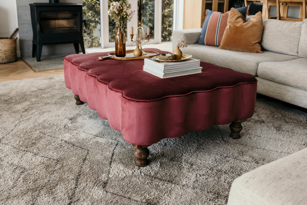 Mauve ottoman in a living room setting with a sofa and decorative items.