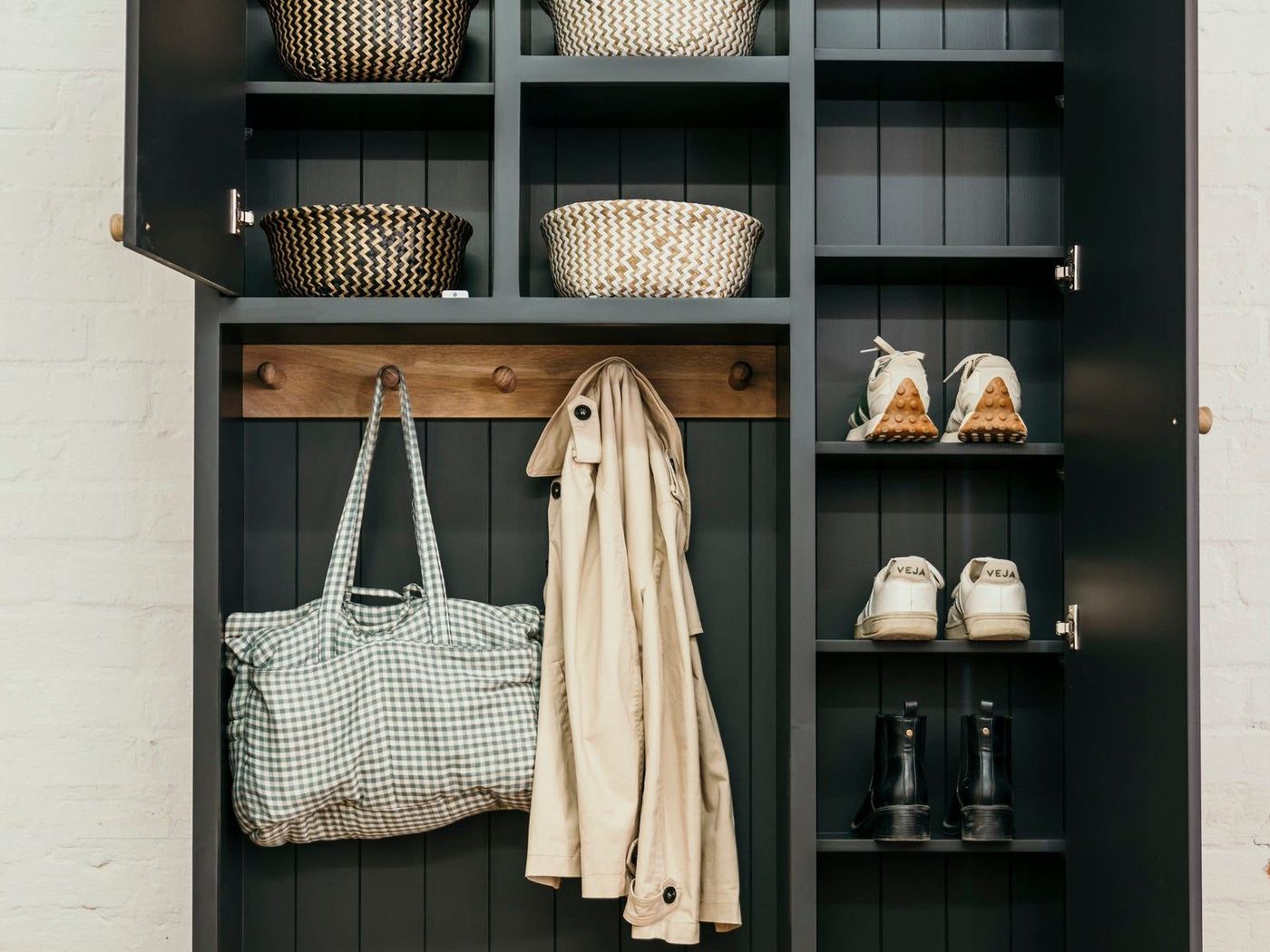 An open mudroom cabinet with coats, shoes and baskets